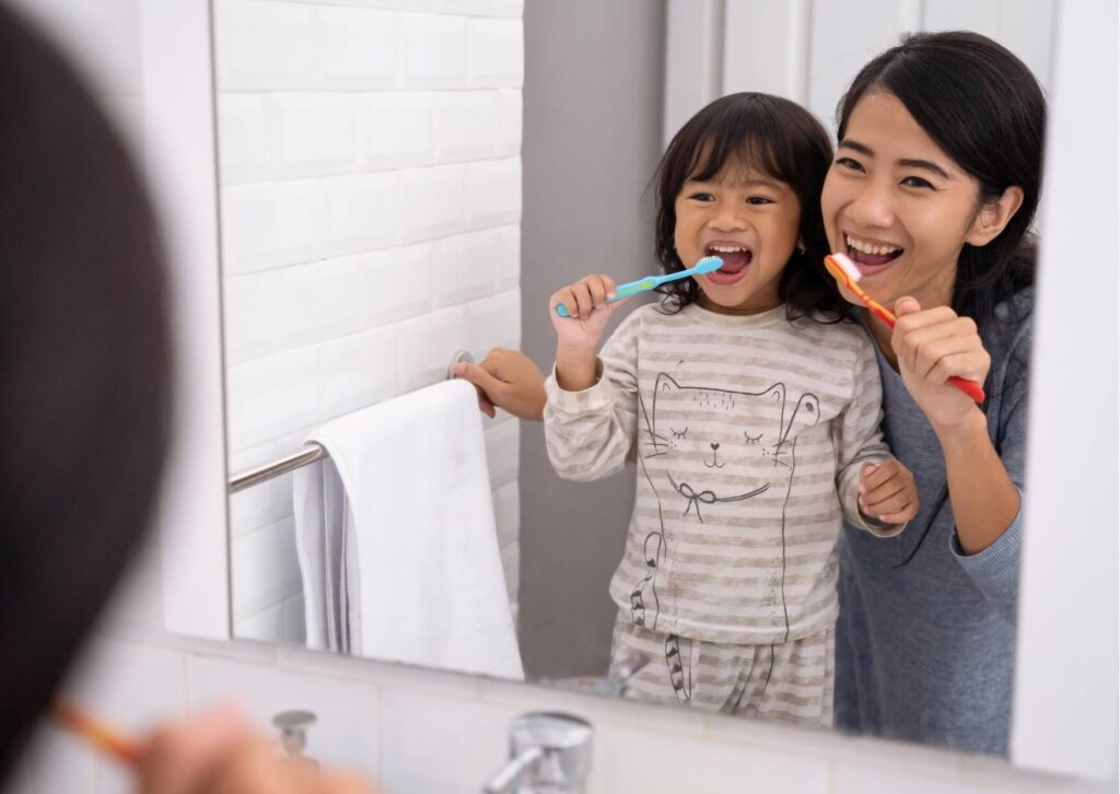 Mother helping her child brush their teeth to prevent cavities from forming over time.
